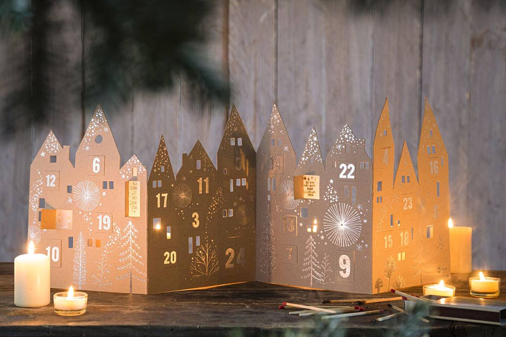 Ein Adventskalender ist mit Kerzen und Lichtern dekoriert auf einer Kommode aufgebaut.