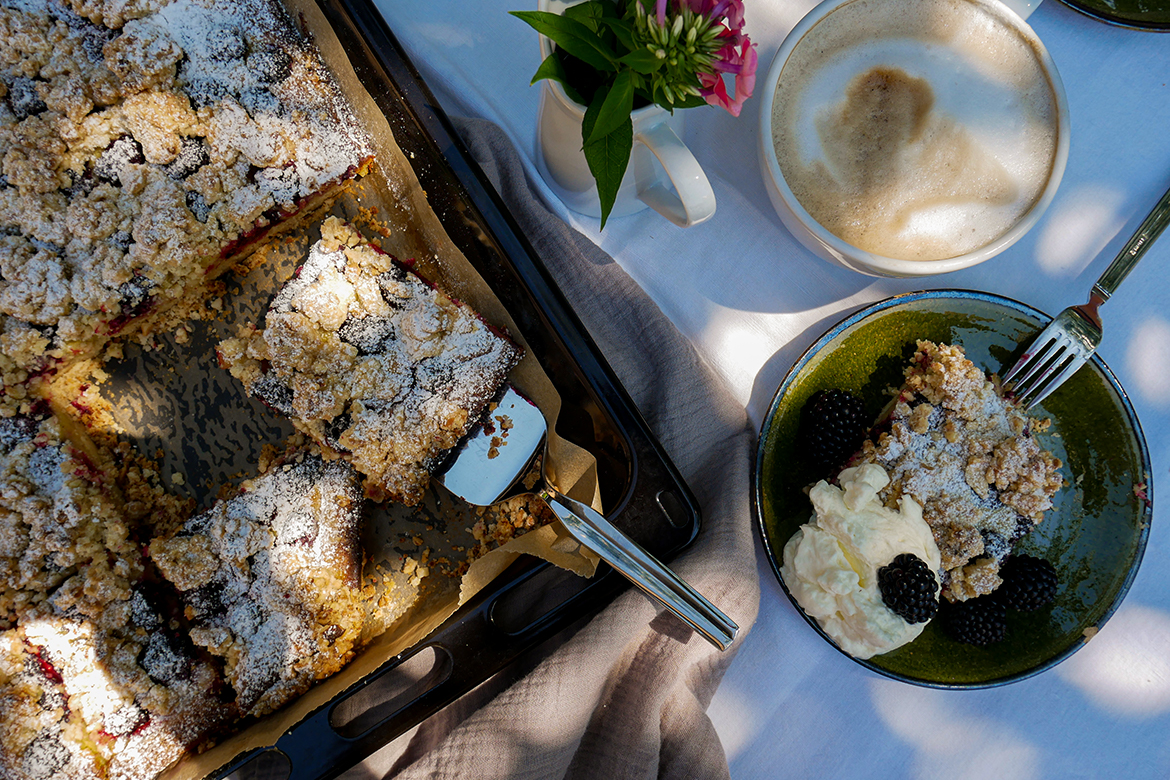 Der Brombeerkuchen vom Blech steht auf einem gedeckten Tisch.