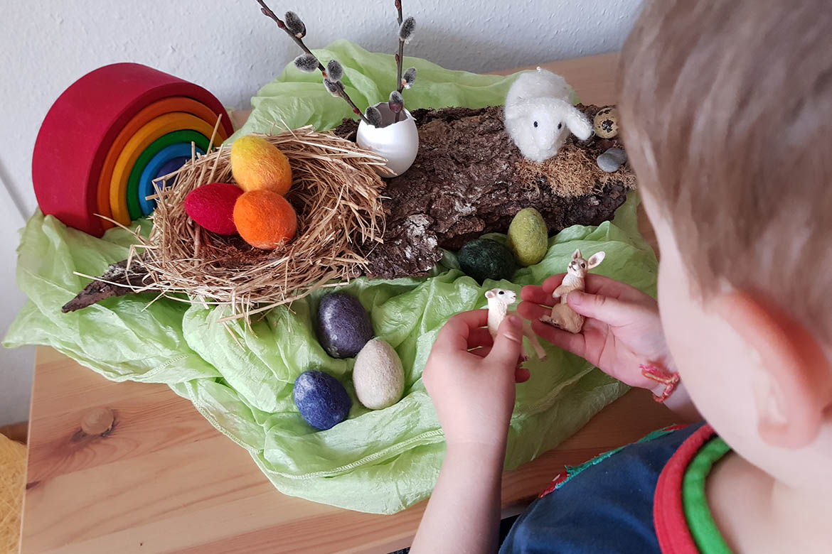 Ein kleiner Junge spielt mit dem Jahrezeitentisch Ostern.