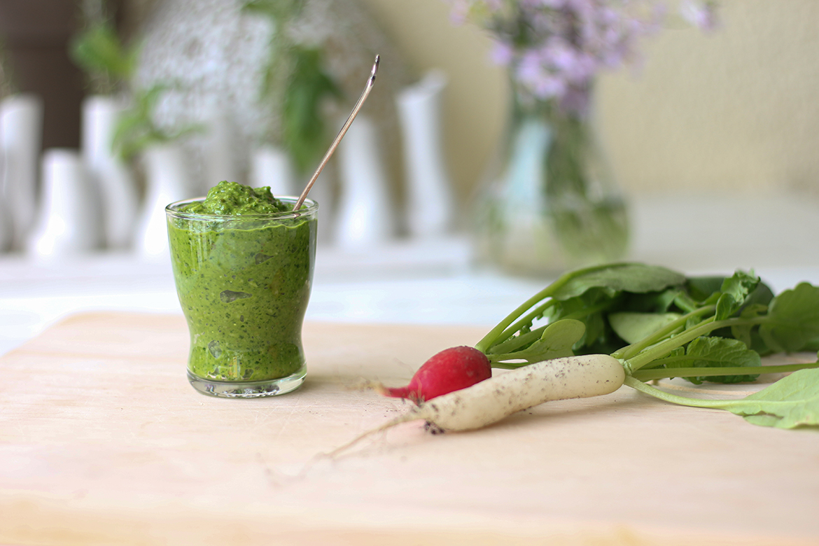 Fertiges Radieschen-Pesto steht in einem Gläschen auf einem Holztablett.