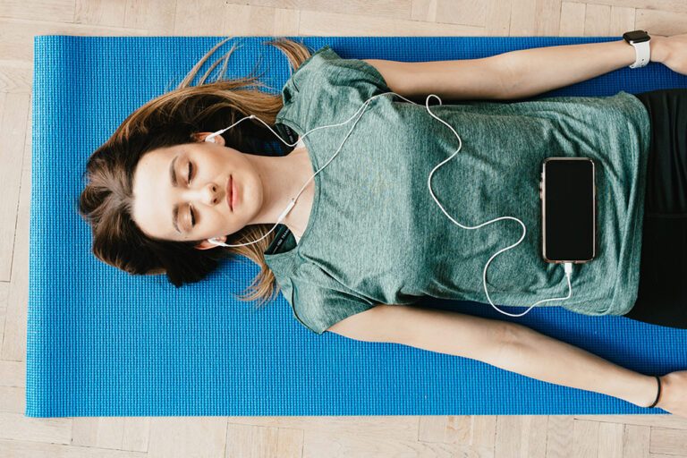 Eine Frau liegt auf einer blauen Sportmatte und führt eine Body-Scan-Meditation durch.