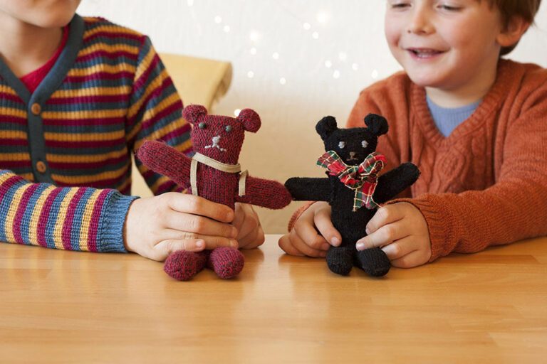 Zwei kleine Kinder spielen mit Teddybären, die aus alten Handschuhen genäht wurden.