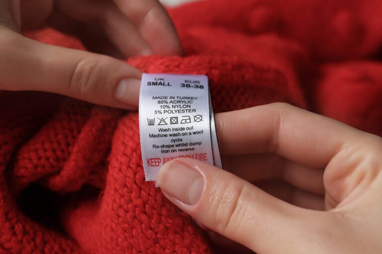 Auf einem Textiletikett eines roten Pullovers sind die Materialien verzeichnet, die das Mikroplastik in der Kleidung nachweisen.