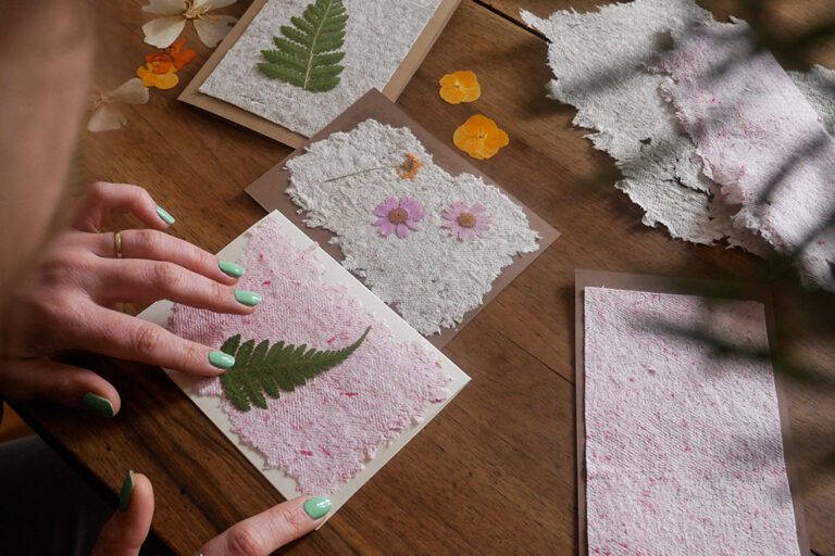 Eine Frau bastelt aus dem handgeschöpftem Papier Karten, die sie mit gepressten Pflanzen verziert.