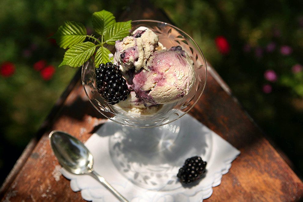 Selbst gemachtes Eis ist in einem Eisbecher aus Glas auf einem Gartentisch angerichtet.