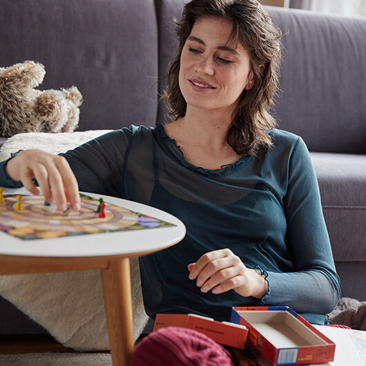 Frau im Bio-Seidenshirt sitzt im Wohnzimmer und spielt ein Brettspiel