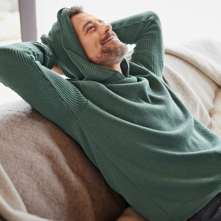 Mann im Bio-Pullover entspannt auf dem Sofa