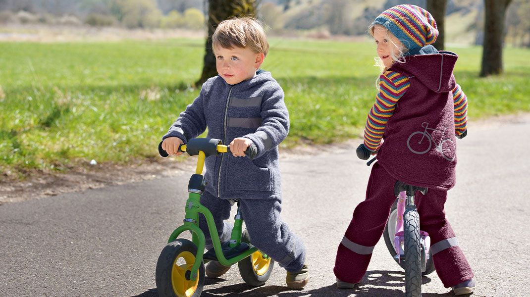 Zwei Kinder auf Laufrädern mit unseren Walkhosen und Walkjacken mit Reflektoren