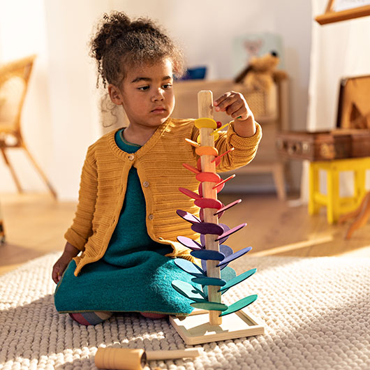 Mädchen spielt mit Murmel und buntem Klangbaum aus Holz