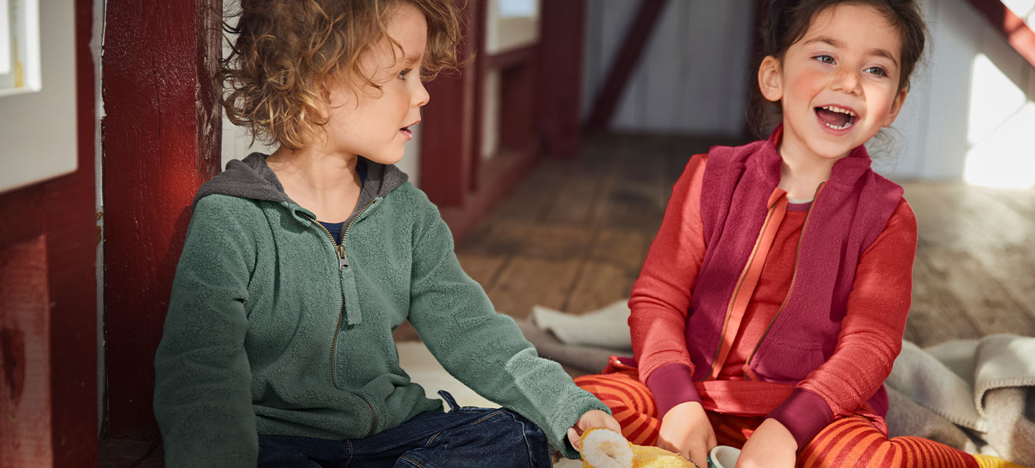 Kinder in gemütlicher Bio-Kindermode spielen auf dem Boden.