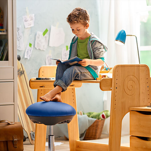 Junge sitzt auf mitwachsendem Kinderschreibtisch in nachhaltig eingerichtetem Kinderzimmer